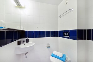 A modern bathroom with white and blue tiles, a white sink, a toilet, and a shower area.