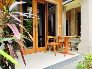 Una puerta de madera con paneles de vidrio, una pequeña mesa de madera y sillas frente a un edificio.