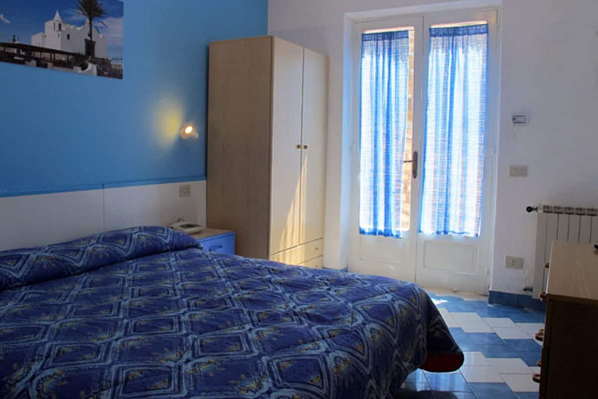 A bedroom with a bed, a wardrobe, a nightstand, and a window with curtains.