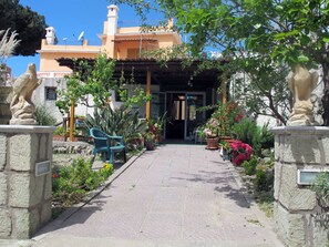 Un camino que lleva a un edificio con entrada cubierta, pilares de piedra y plantas en macetas.