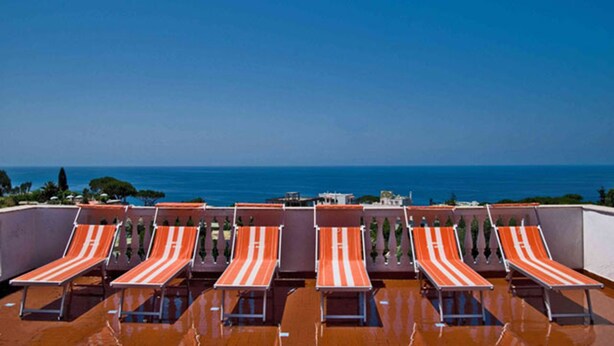 Une terrasse sur le toit, dotée de six chaises longues à rayures, donnant sur une mer bleue et limpide.