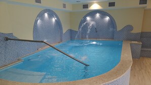 Une piscine intérieure avec un revêtement de carrelage, un escalier en métal et un mur également recouvert de carrelage, orné d’un motif ondulé.