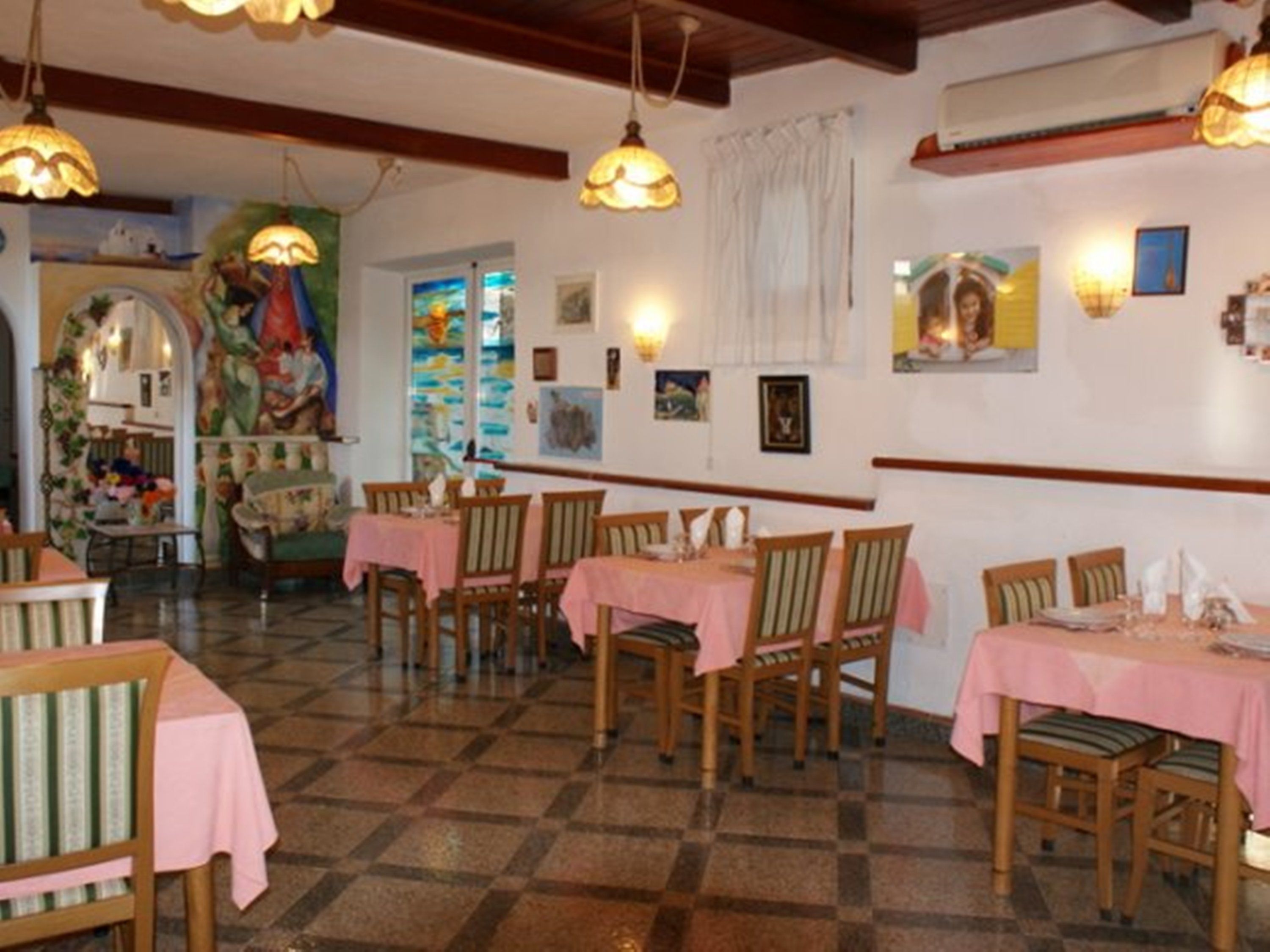A dining area with wooden tables and chairs, pink tablecloths, and wall-mounted light fixtures.