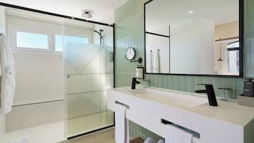 A modern bathroom with a glass-enclosed shower, a large mirror, and a white vanity with a black faucet.