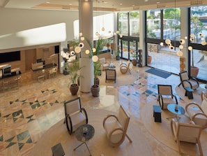 A spacious lobby with a modern design, featuring a mix of seating areas, a reception desk, and large windows offering views of the outdoors. - H10 Costa Mogán (Mogan)