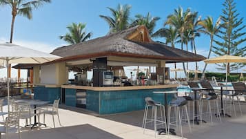 Un espace bar extérieur doté d’un toit de chaume, de sièges et offrant une vue sur la piscine.