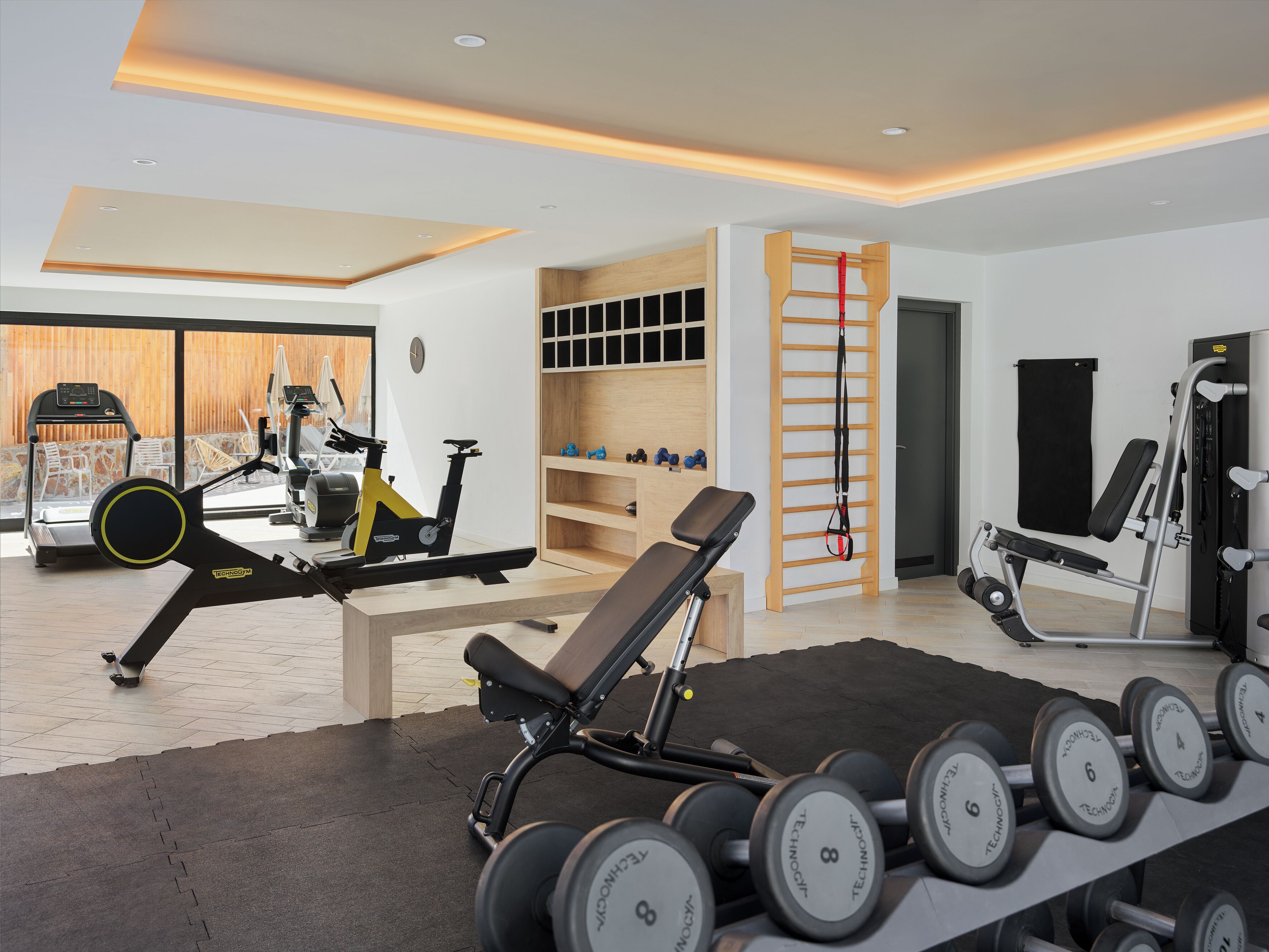Une salle de sport moderne pour la maison, équipée d’appareils d’exercice, d’un banc et d’un porte-haltères.