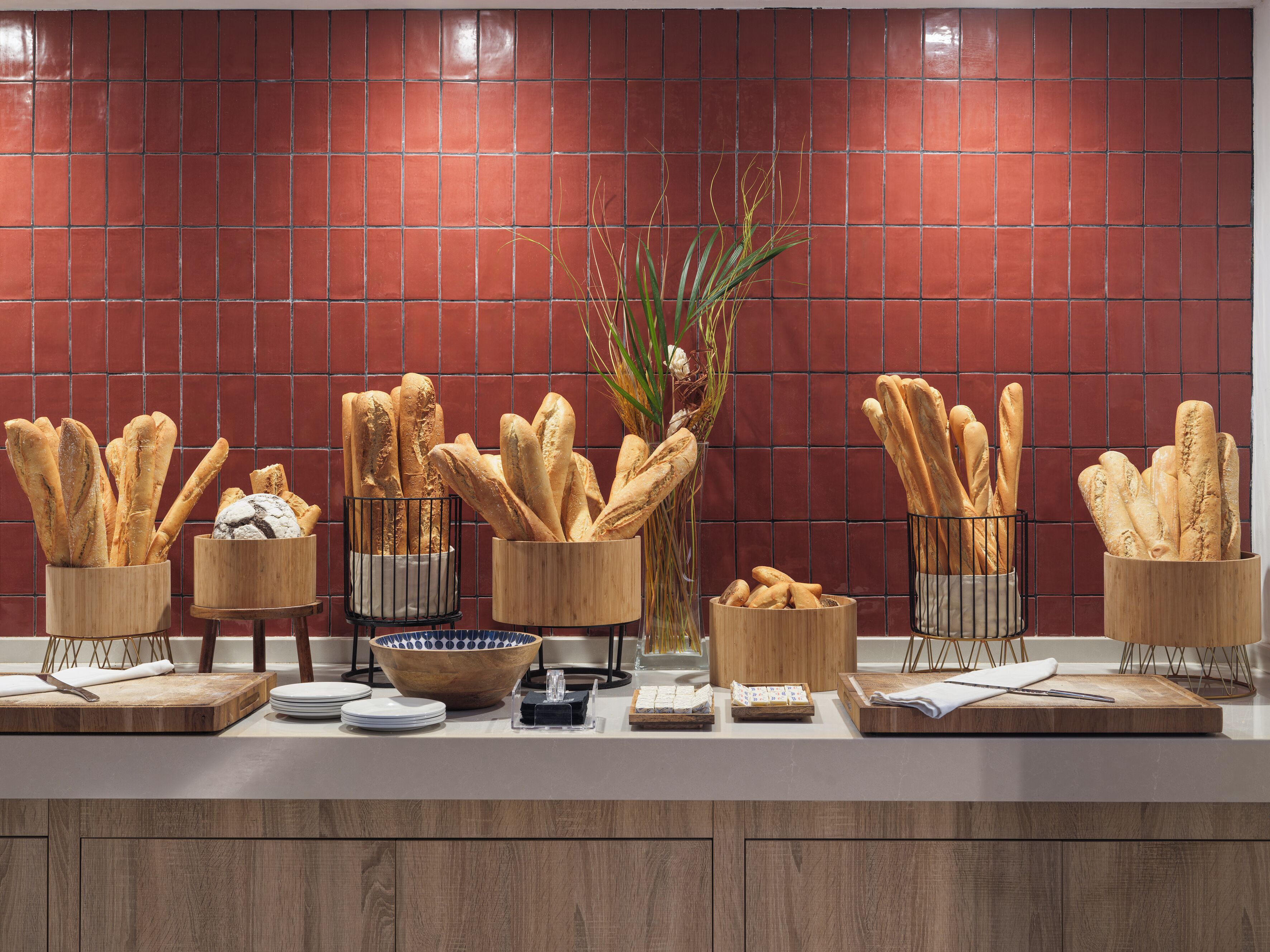 Una encimera de cocina con diferentes tipos de pan en recipientes de madera, un cuenco de madera y un florero con plantas.