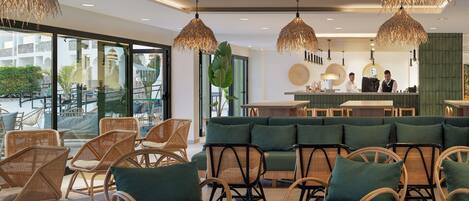 A modern interior with wicker furniture, a bar area, and large windows offering views of the outdoors.