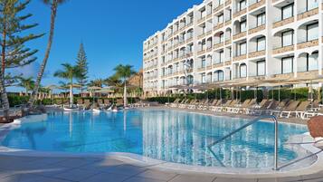 Un hotel con una piscina grande, tumbonas y palmeras.