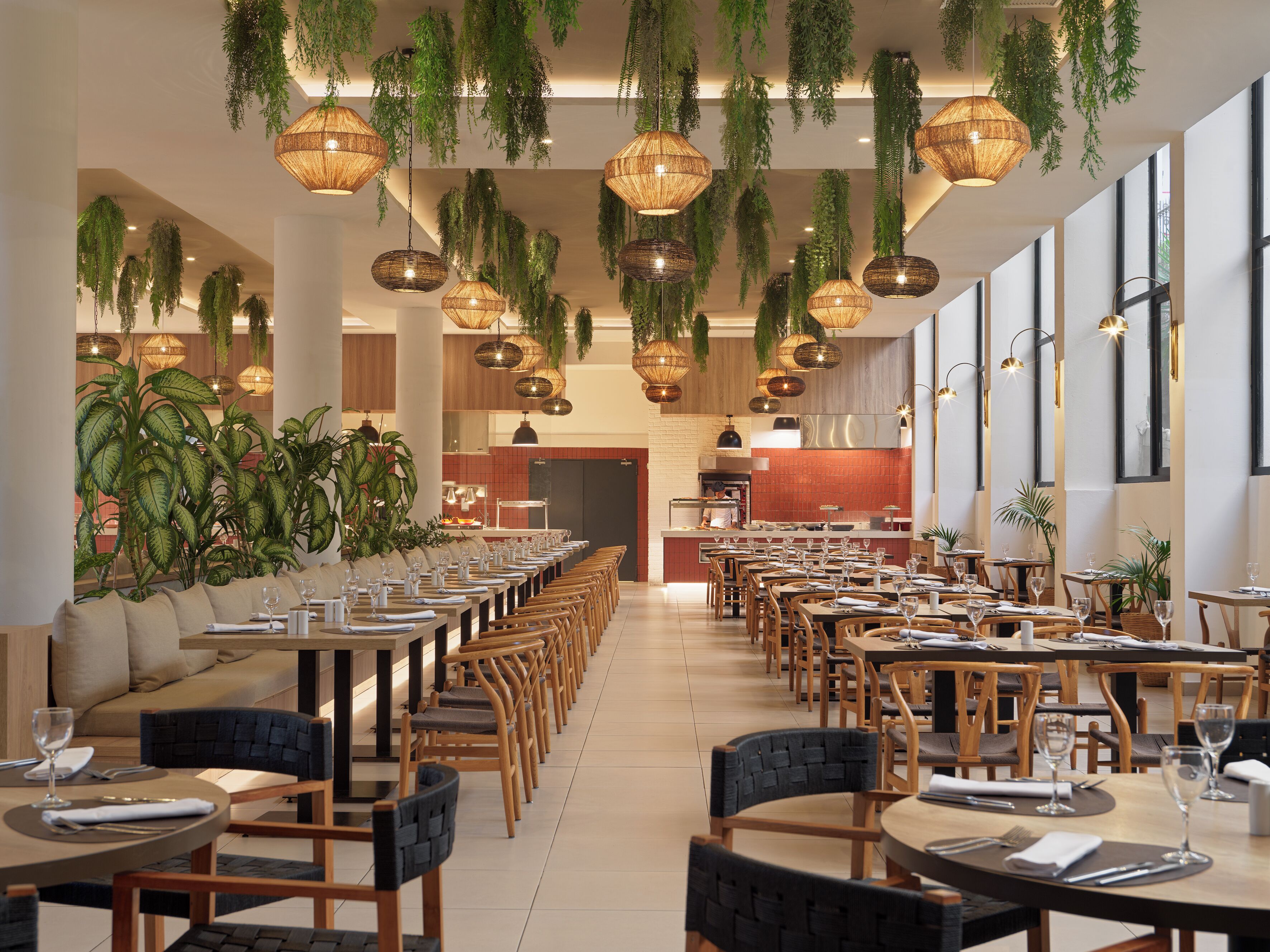 Un restaurante espacioso con largas mesas de comedor, plantas colgantes e iluminación cálida.