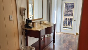 A bathroom with a vanity, a large mirror with lights, a hairdryer, and a trash can. - Drama Inn (Cherokee)