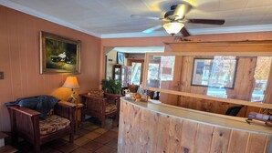 A room with a wooden reception desk, a ceiling fan, a painting on the wall, and a tiled floor. - Drama Inn (Cherokee)
