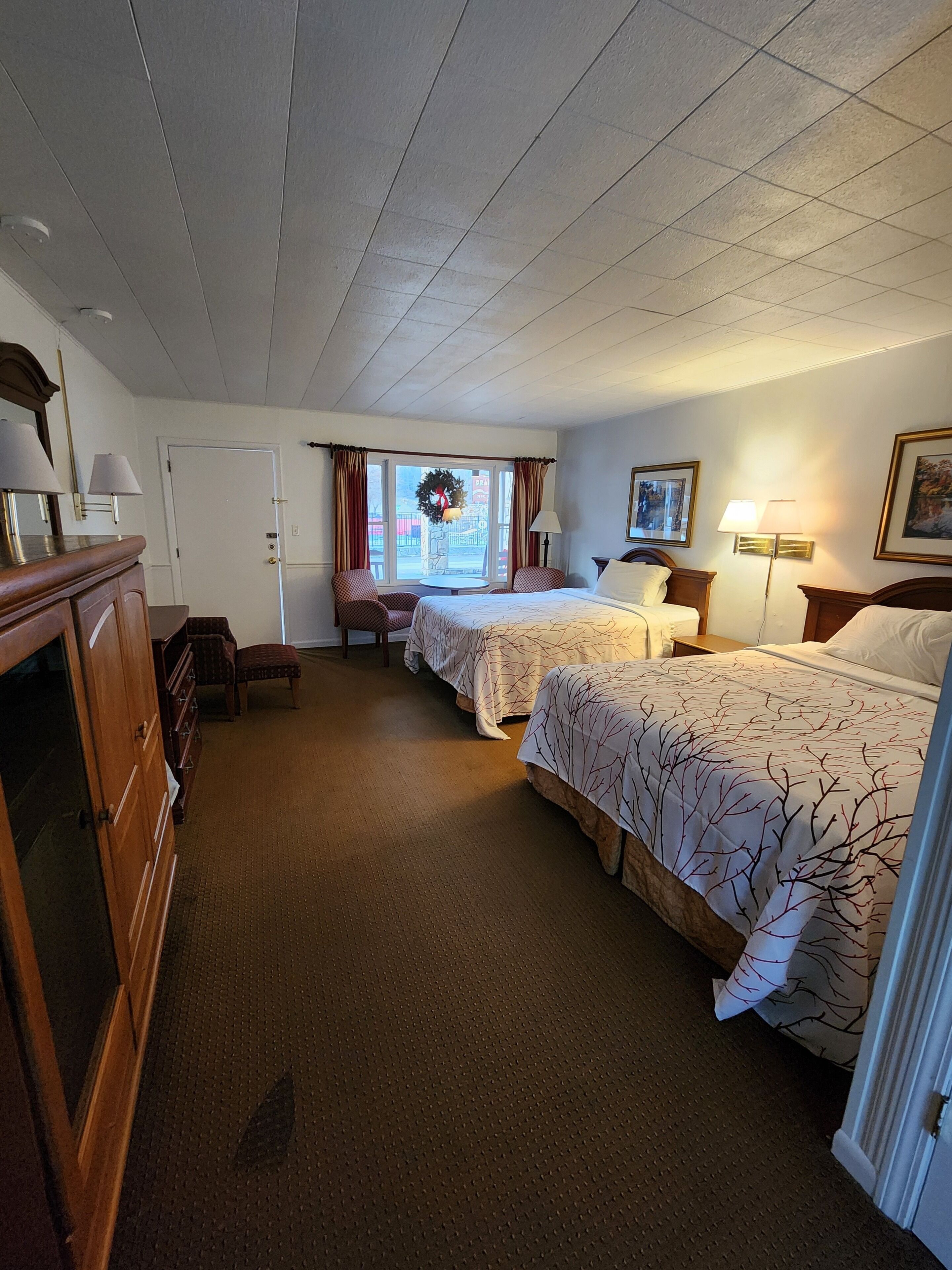 A hotel room with two beds, a wooden dresser, a small table, and a window with a wreath.