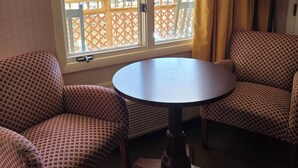 A room with a round table and two patterned chairs, a window with yellow curtains, and a view of a wooden deck and trees. - Drama Inn (Cherokee)