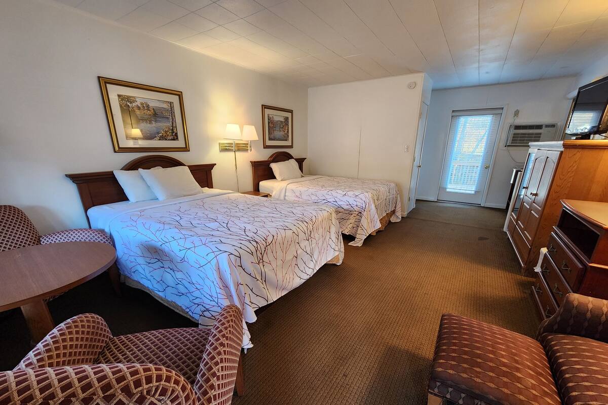A hotel room with two beds, a desk, a chair, a dresser, and a television.