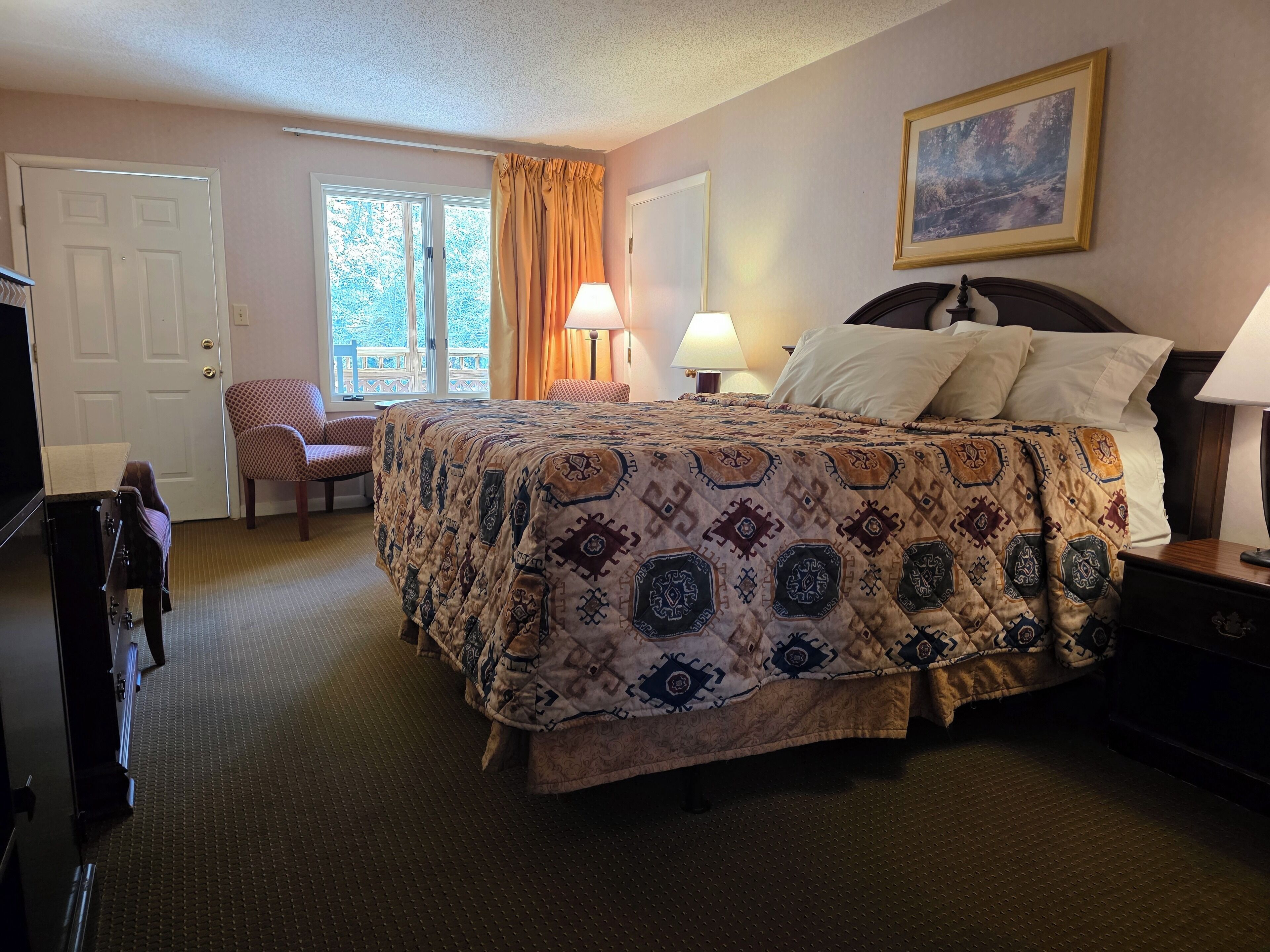 Une chambre d’hôtel avec un grand lit, deux lampes de chevet, une chaise, un bureau et un téléviseur.