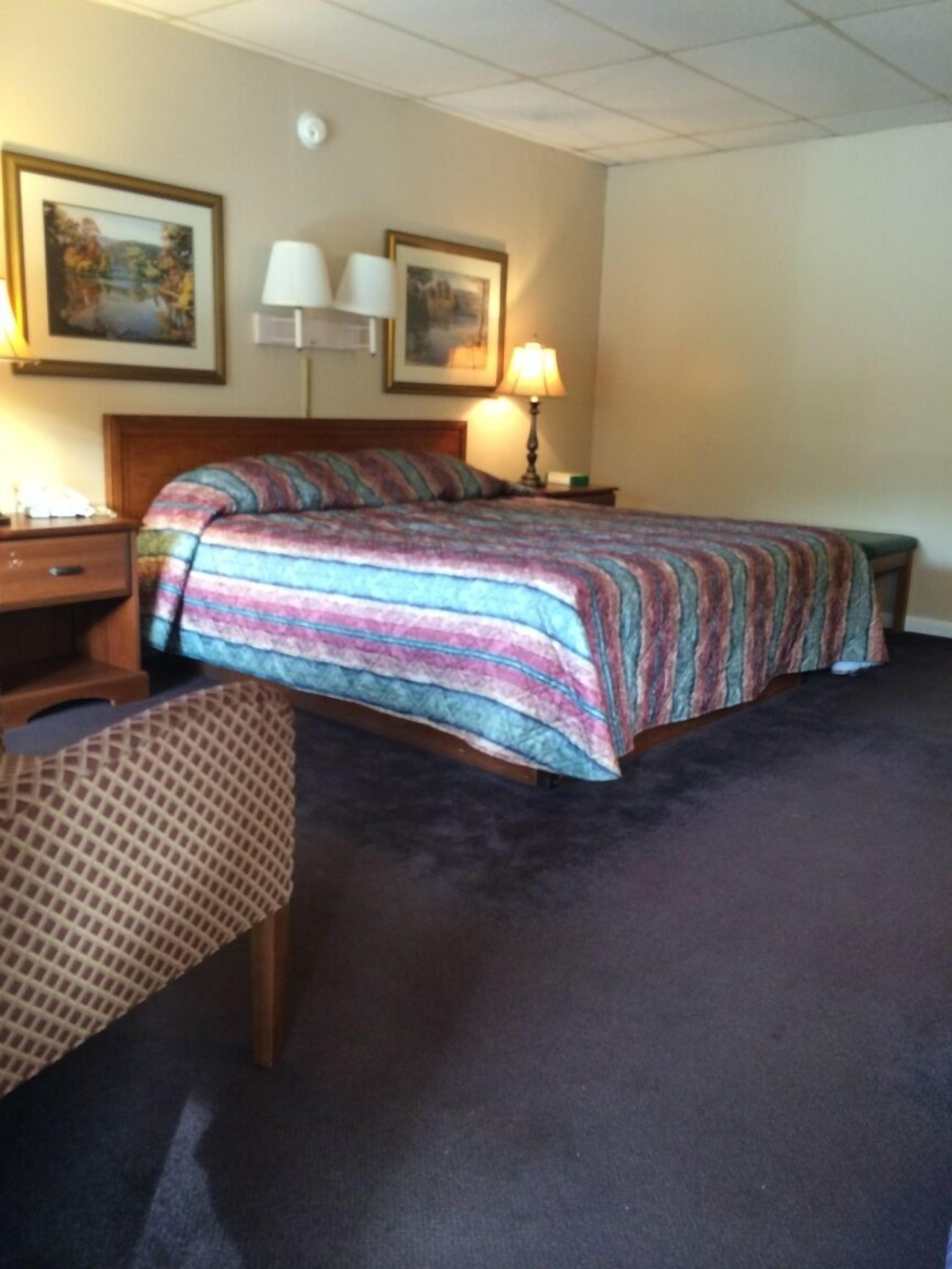 Een hotelkamer met een bed, een bureau, twee lampen en twee ingelijste foto's aan de muur.