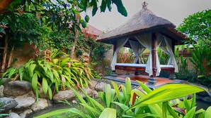 Um gazebo com telhado de palha rodeado por vegetação exuberante e um pequeno lago.