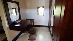 Quarto com um banco de madeira, uma mesa pequena, um espelho e um guarda-roupa.