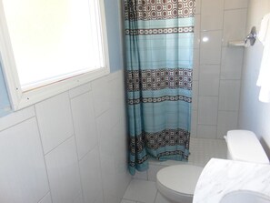 A small bathroom with a toilet, a window, and a shower curtain. - Westbrook Motel (Abbeville)