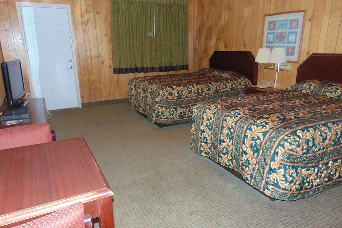 A hotel room with two beds, a desk, a television, and a window with curtains.