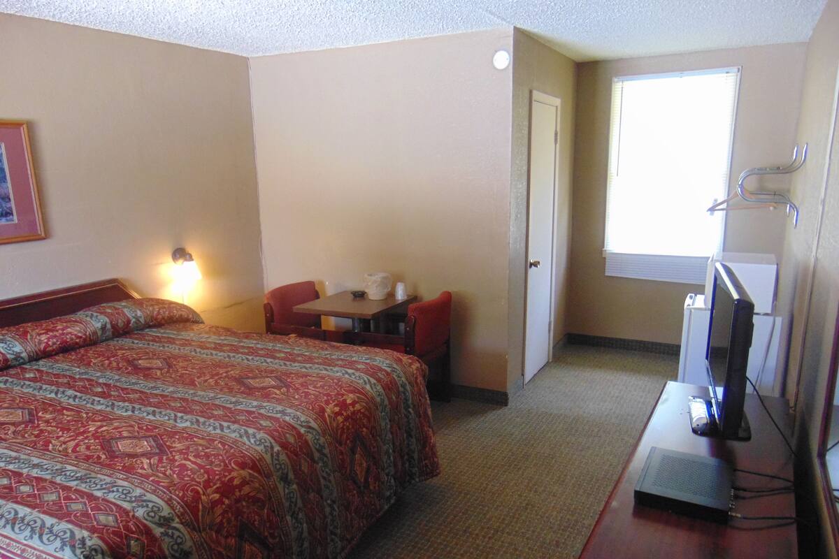 A hotel room with a large bed, a desk, a chair, a television, and a window.