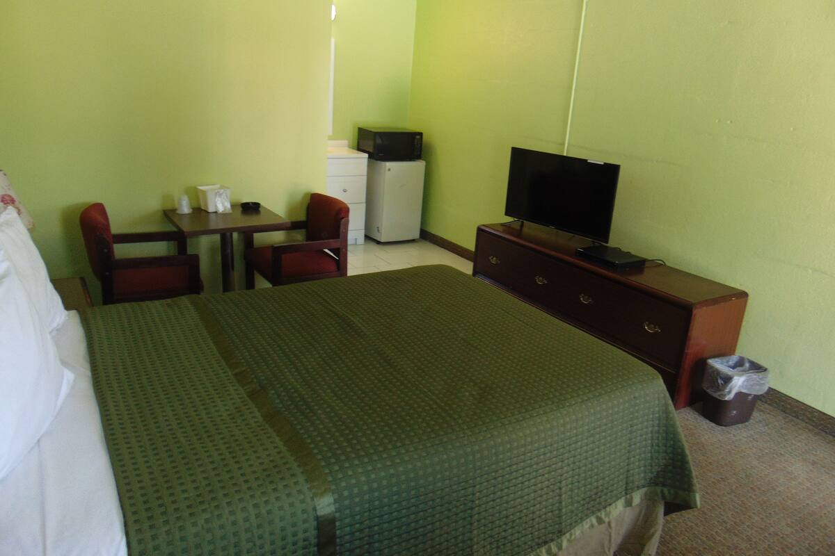 A hotel room with a bed, a desk, a chair, a television, and a small refrigerator.