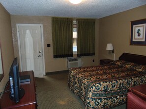 A hotel room with a bed, a desk with a television, a window with curtains, and a framed picture on the wall. - Westbrook Motel (Abbeville)