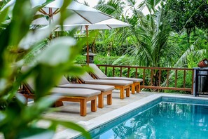 A poolside area with lounge chairs and umbrellas, surrounded by lush greenery. - Pesantian Villa & Warung (Ubud)