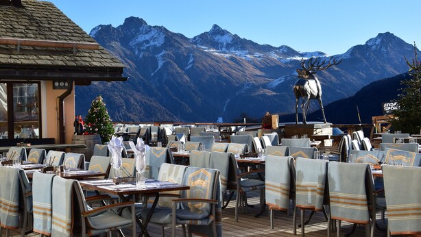 A restaurant with outdoor seating, tables, chairs, and a mountain view. - Hotel Salastrains (St. Moritz)