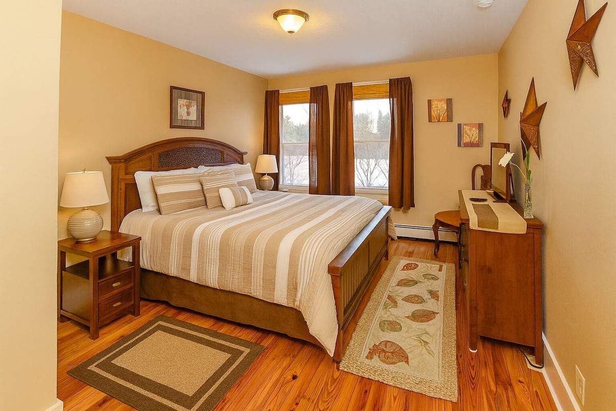 A bedroom with a large bed, wooden nightstands, a dresser, and a window with curtains.