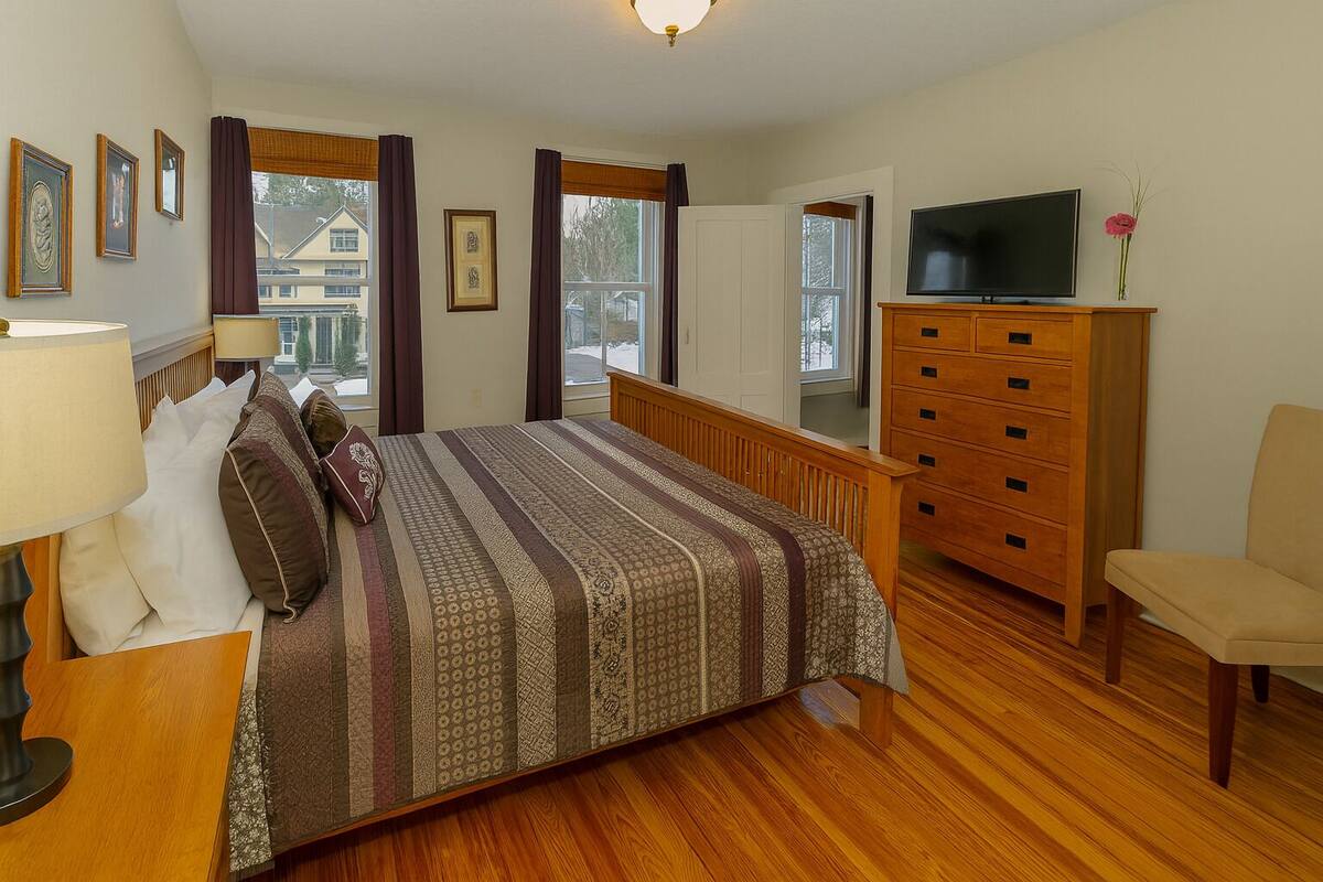 A bedroom with a bed, dresser, TV, and a chair.