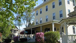 A two-story yellow house with a porch, surrounded by greenery and a clear sky. - Lakeview Inn (Naples)