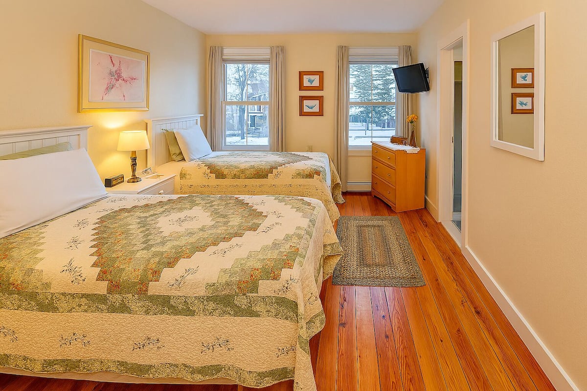 A bedroom with two beds, a dresser, a TV, and a window with curtains.