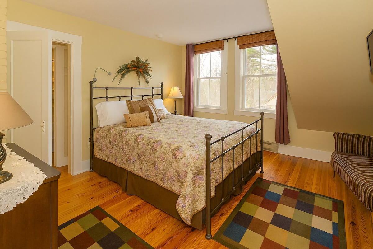 A bedroom with a bed, bedside table, lamp, and a chair.