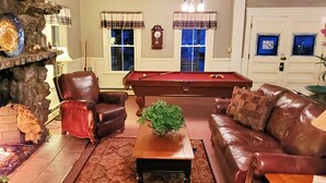 A cozy living room with a pool table, leather chairs, a fireplace, and a clock on the wall. - Lakeview Inn (Naples)