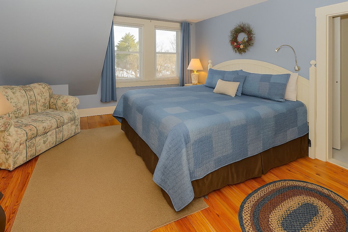 A bedroom with a bed, a sofa, a window, a lamp, and a rug.