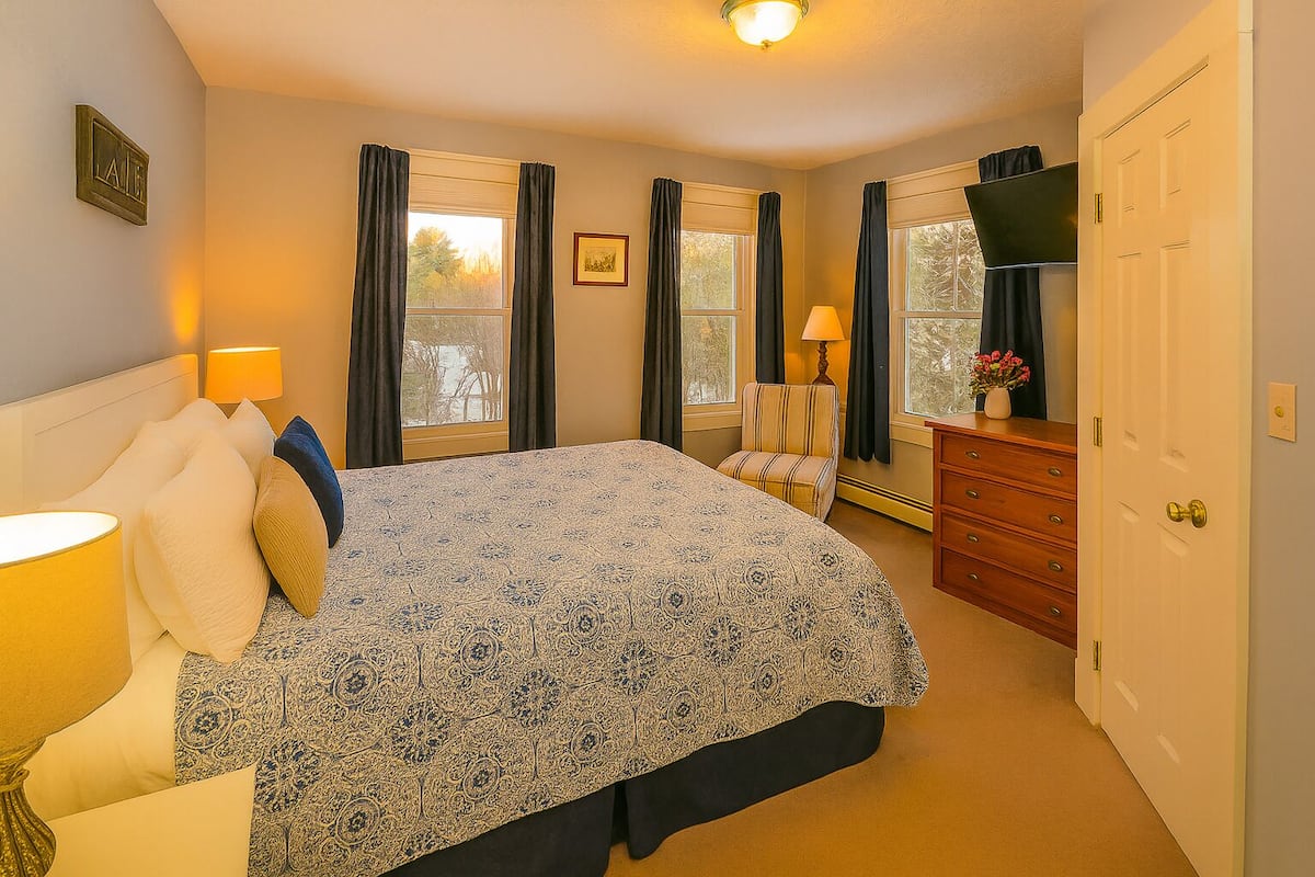 A bedroom with a bed, bedside lamps, a dresser, a chair, and a door.