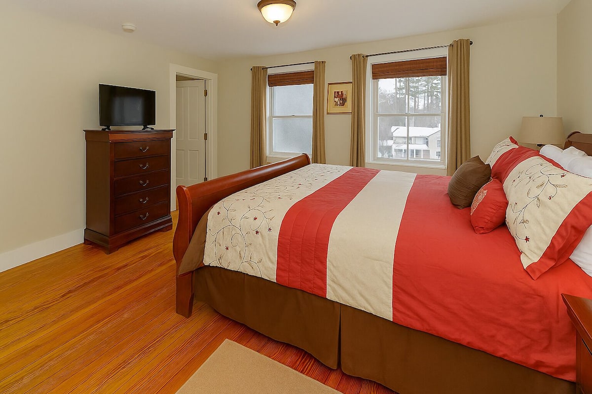 A bedroom with a wooden bed, a dresser, a television, and a window with curtains.