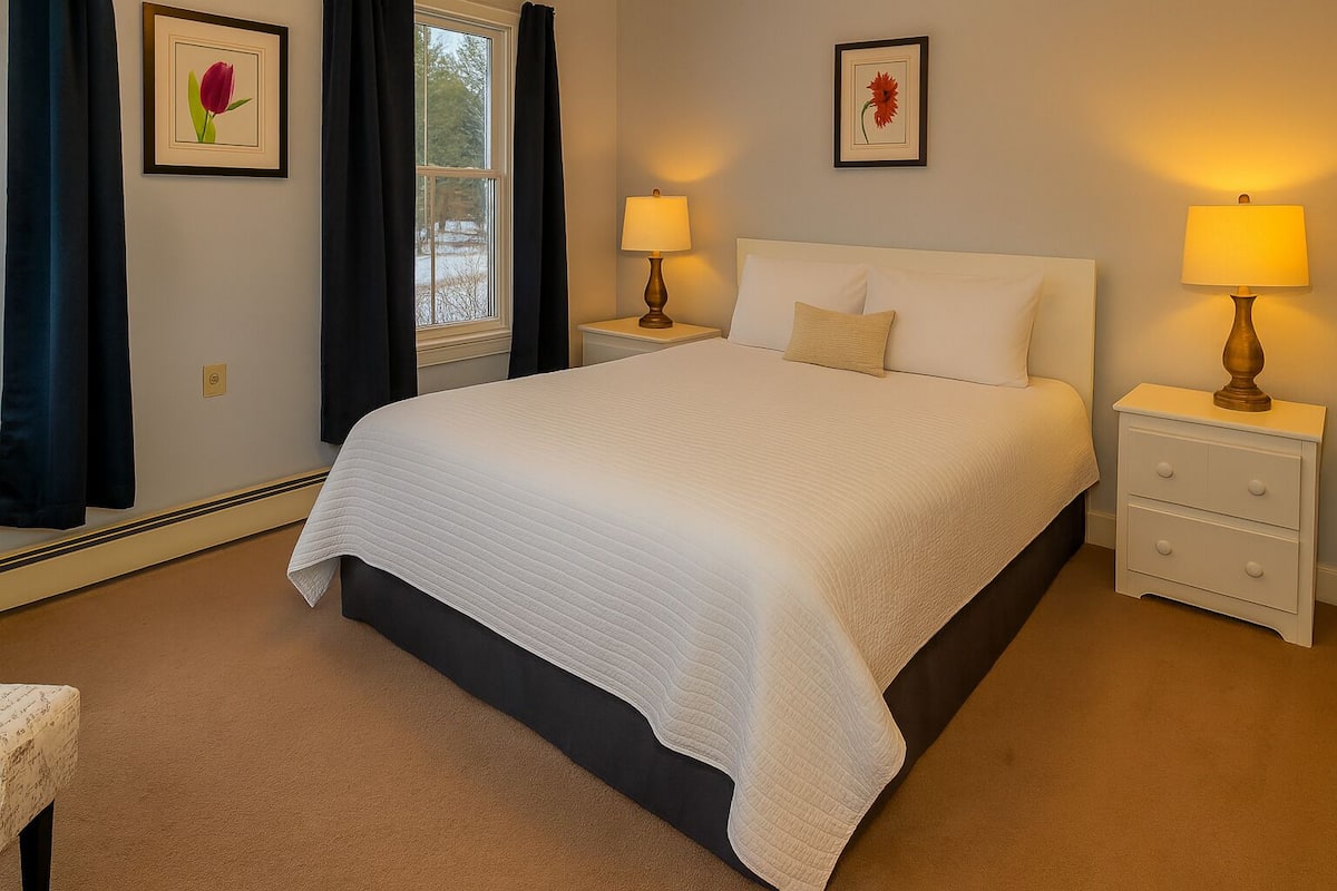 A neatly arranged bedroom with a large bed, two bedside tables with lamps, and two framed floral pictures on the walls.