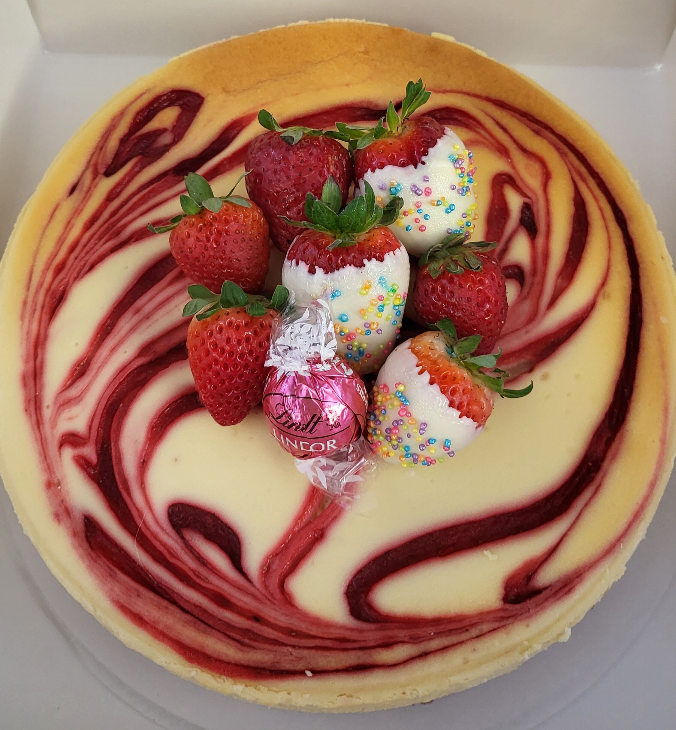 A cheesecake with strawberries and Lindor chocolates on top.