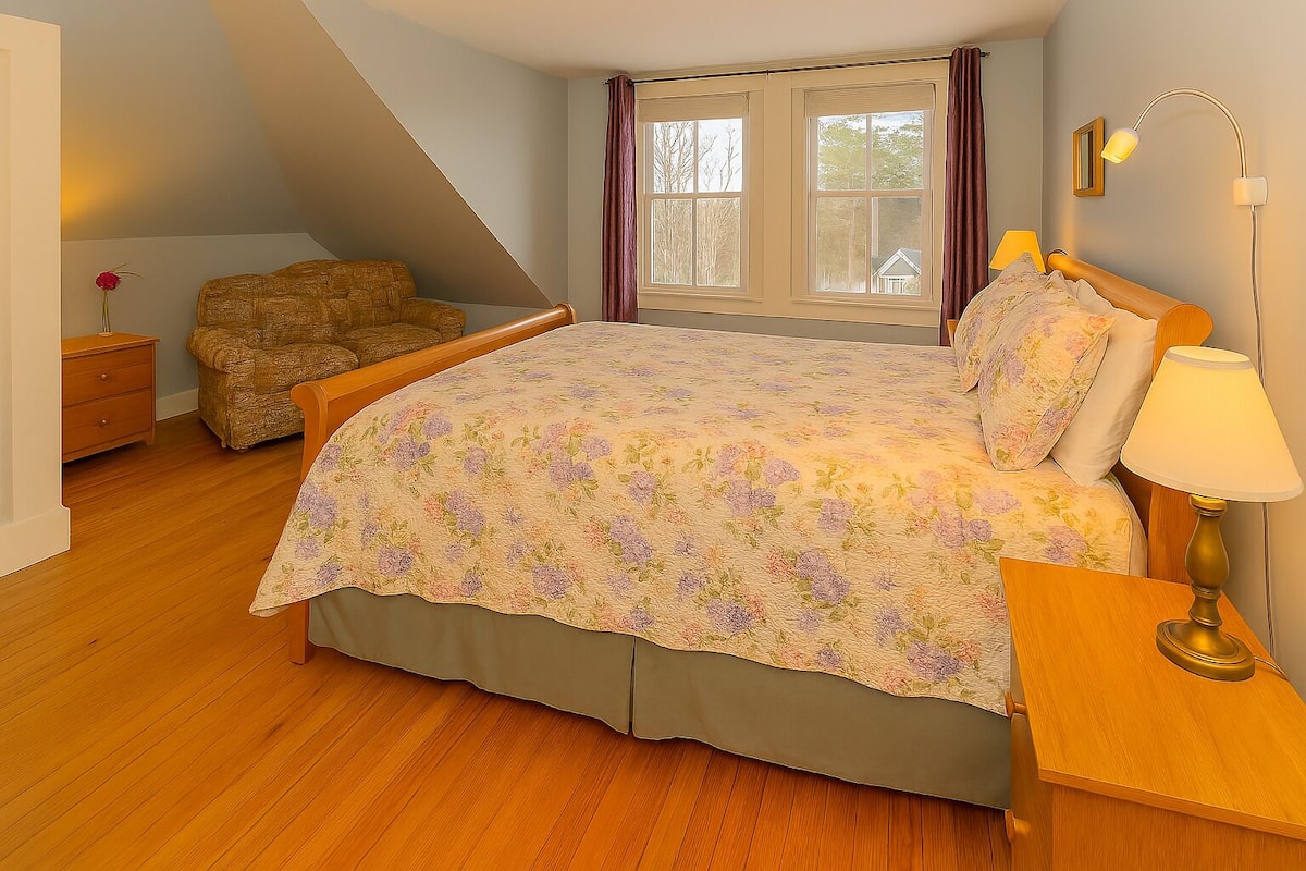 A bedroom with a bed, a nightstand, a lamp, a chair, and a window with curtains.