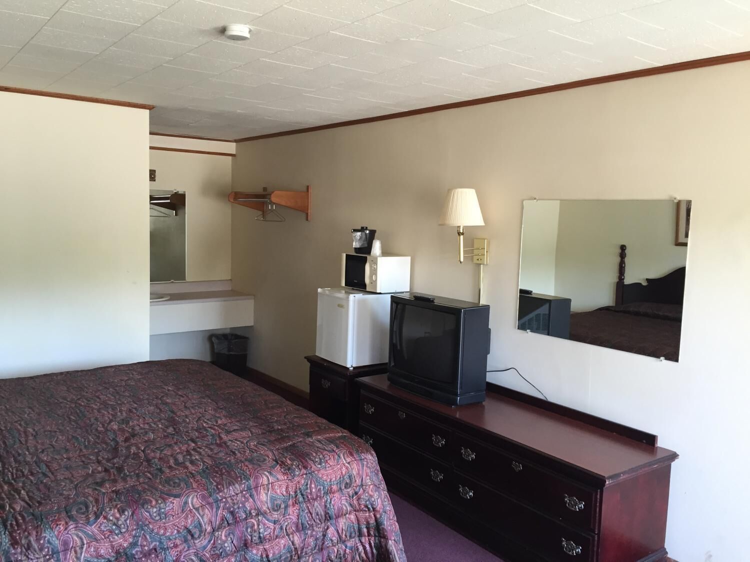 A hotel room with a bed, a dresser, a television, a lamp, and a mirror.
