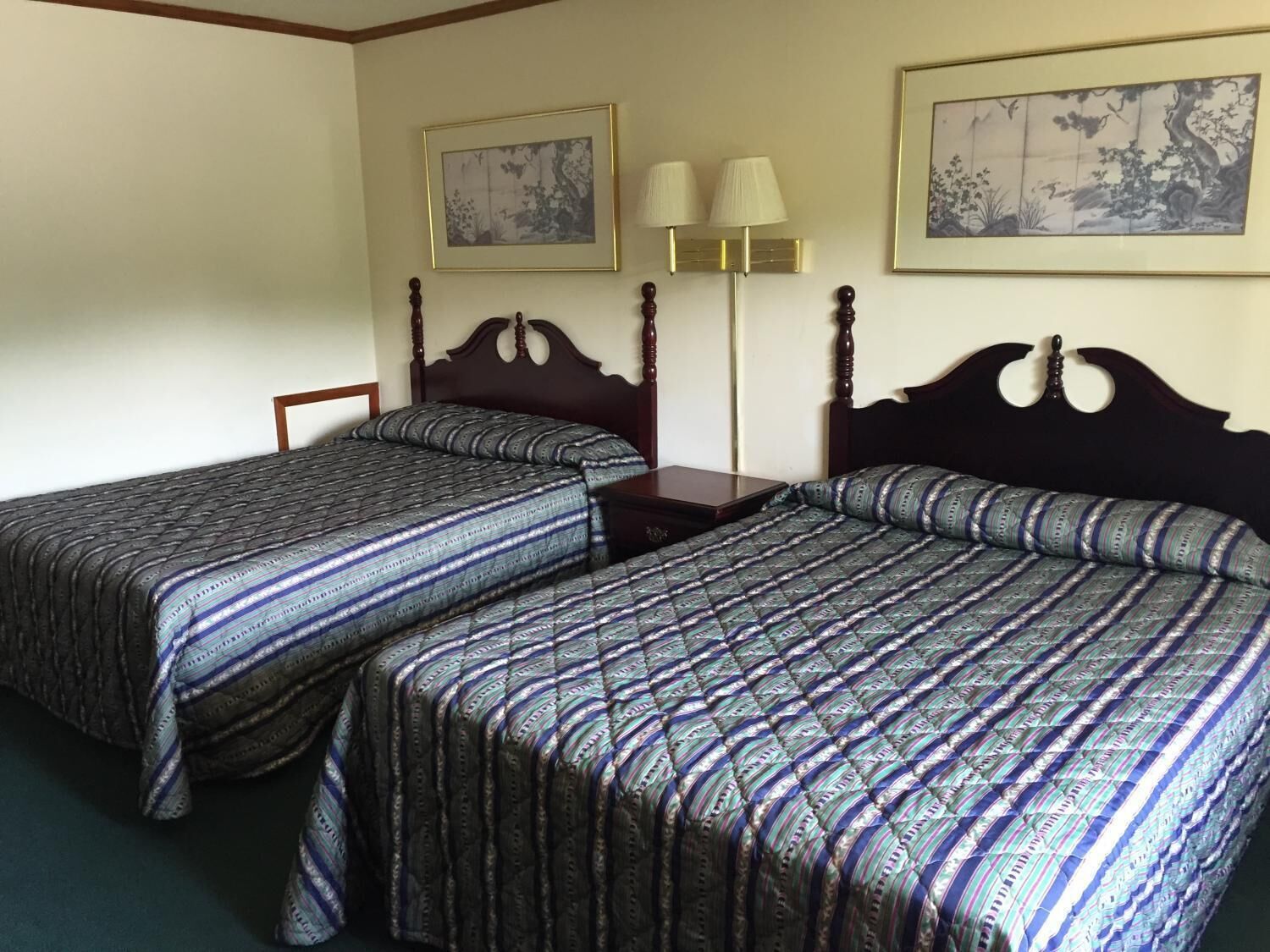 Habitación de hotel con dos camas individuales, una mesita de noche, una lámpara y dos obras de arte enmarcadas en las paredes.