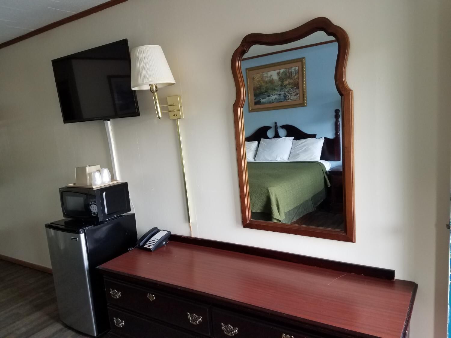 Een hotelkamer met een bed, een dressoir, een televisie, een lamp en een spiegel.