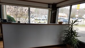 A reception area with a wooden counter, a potted plant, and a view of parked cars outside. - Sapphire Inn (Franklin)