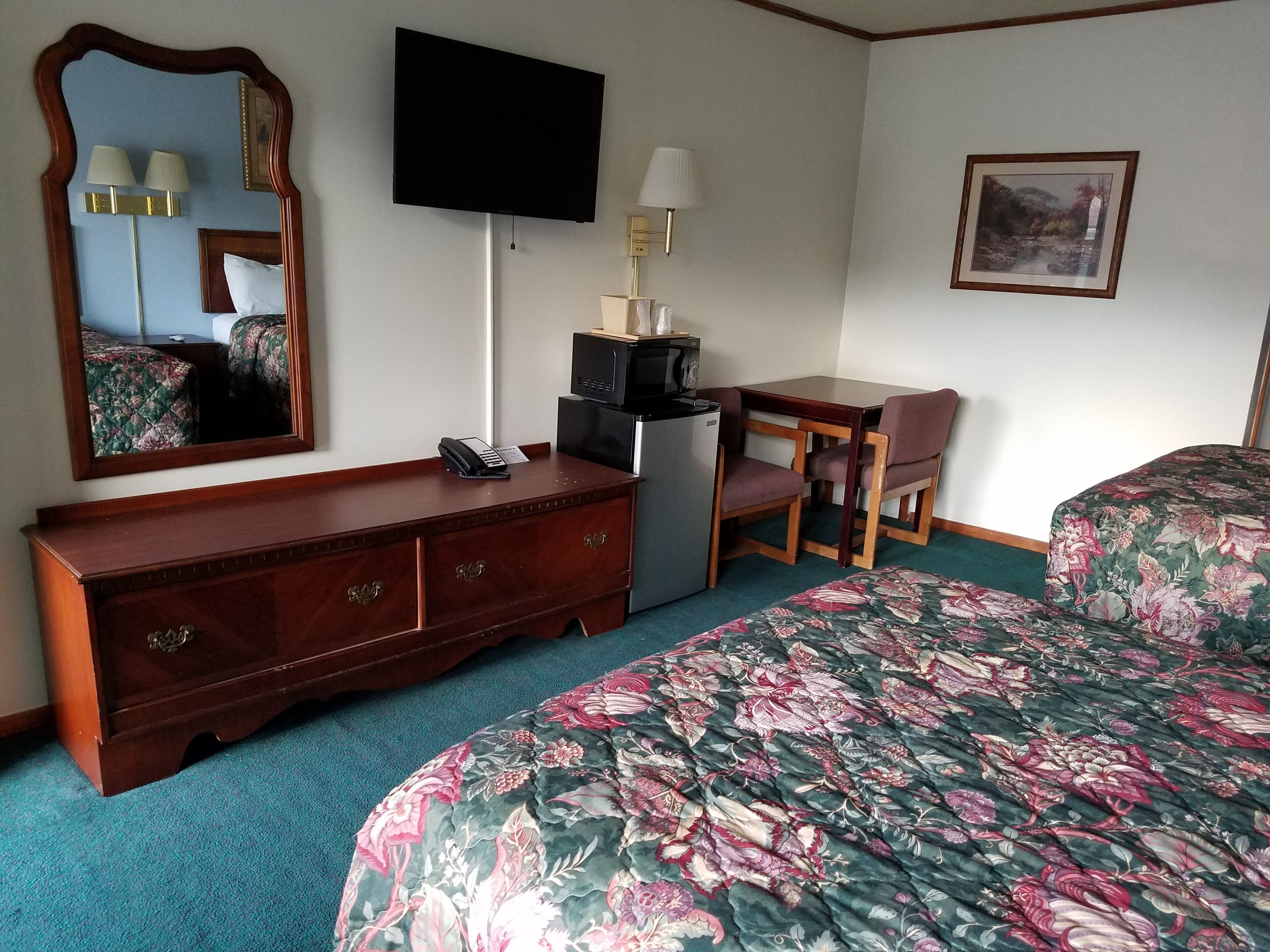 A hotel room with a bed, a desk with a chair, a television, a mirror, a dresser, and a microwave.