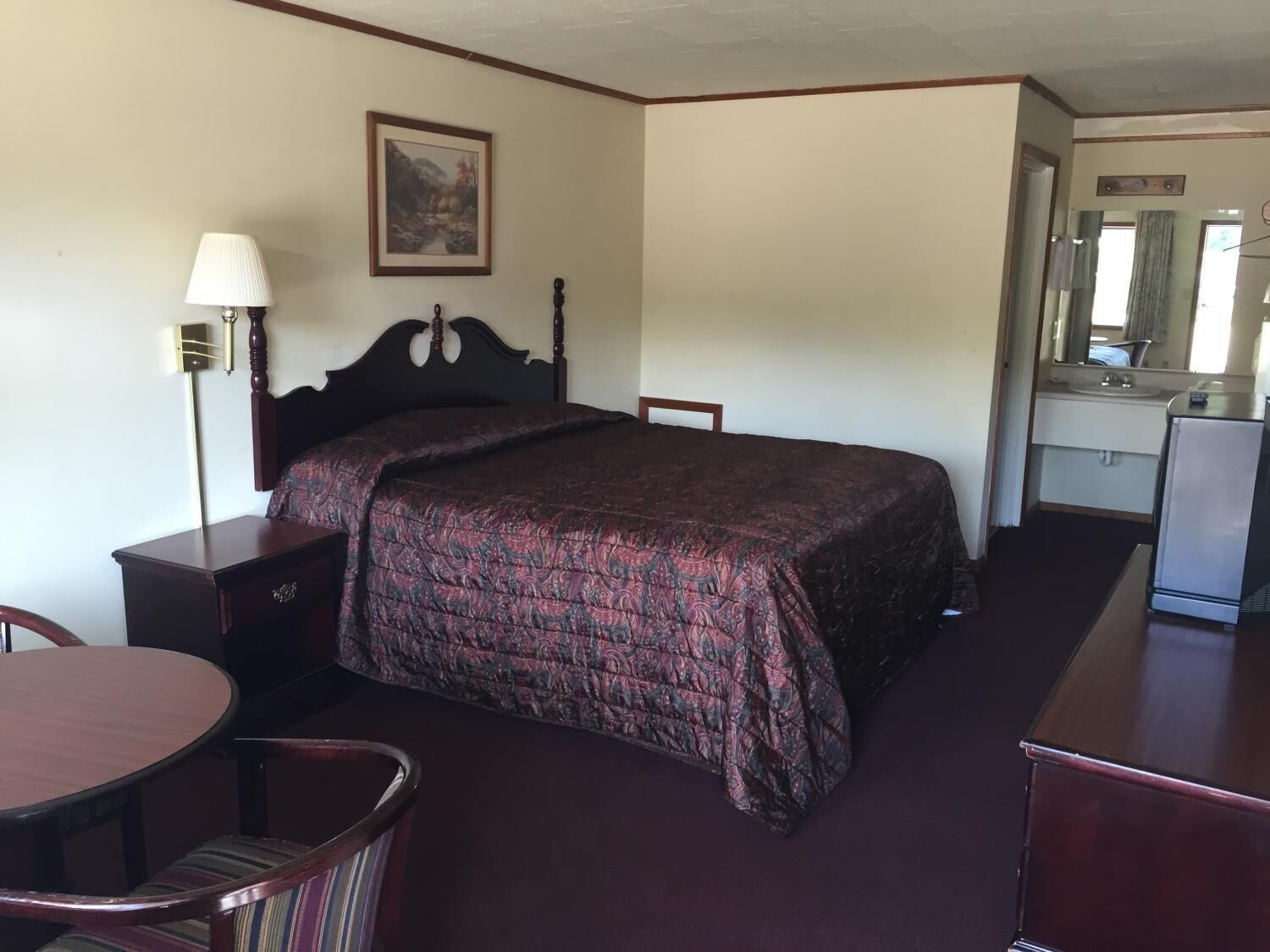 Ein Hotelzimmer mit Bett, Schreibtisch, Stuhl, Lampe, Kommode und Spiegel.