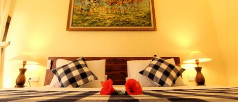 Habitación de hotel con cama, almohadas a cuadros, un cuadro sobre la cama y dos lámparas a cada lado.